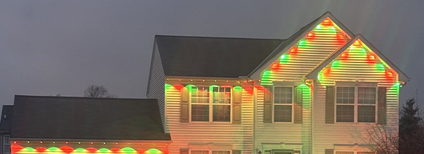 Red and green holiday lights illuminate a home’s gables and garage roofline