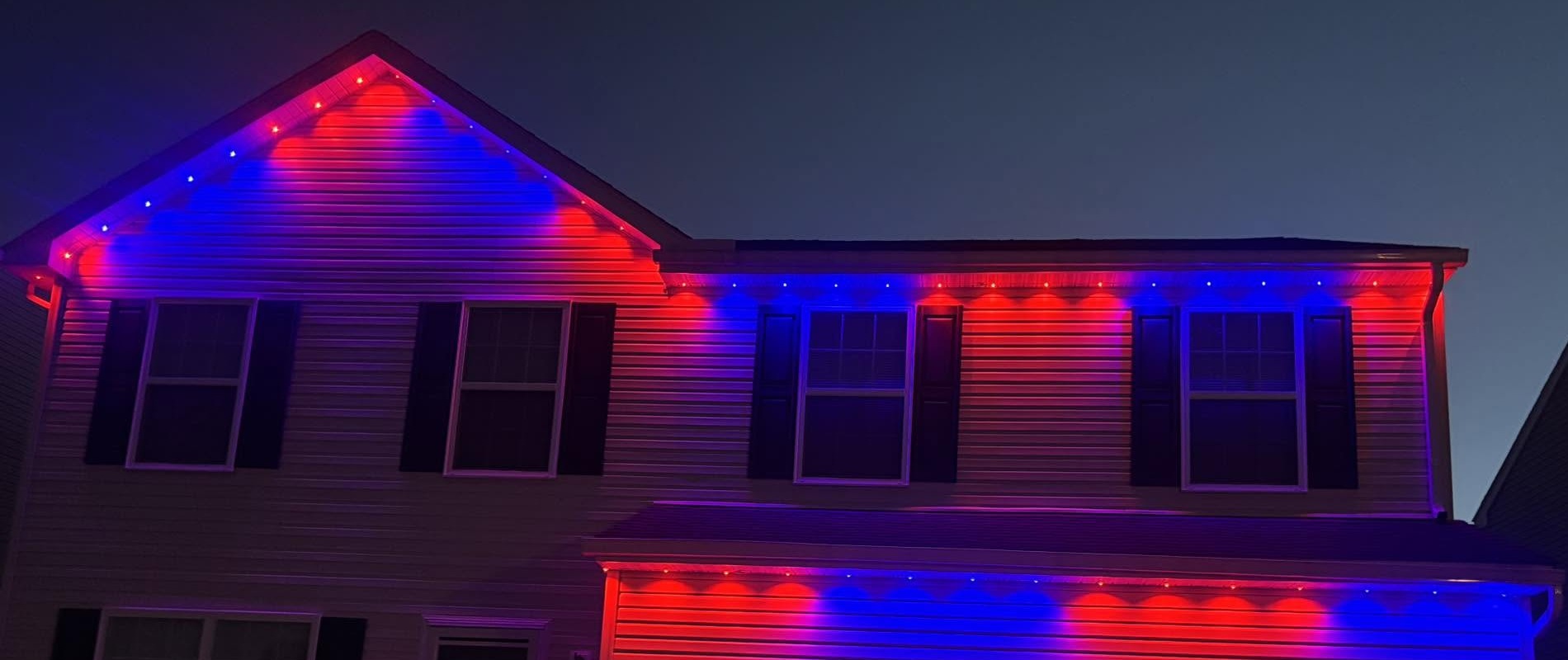 Red and blue outdoor lights illuminate a home’s upper roofline and garage eaves